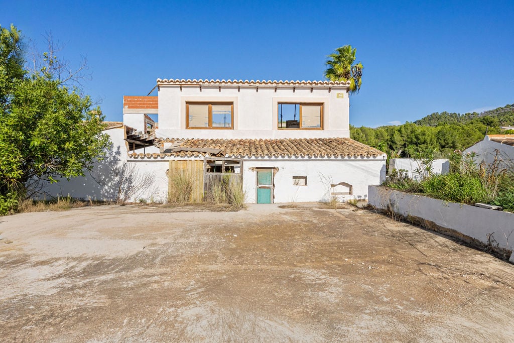 Traditional white-walled structure featuring wooden window frames and terracotta tiling, set on a spacious level plot with surrounding Mediterranean greenery.