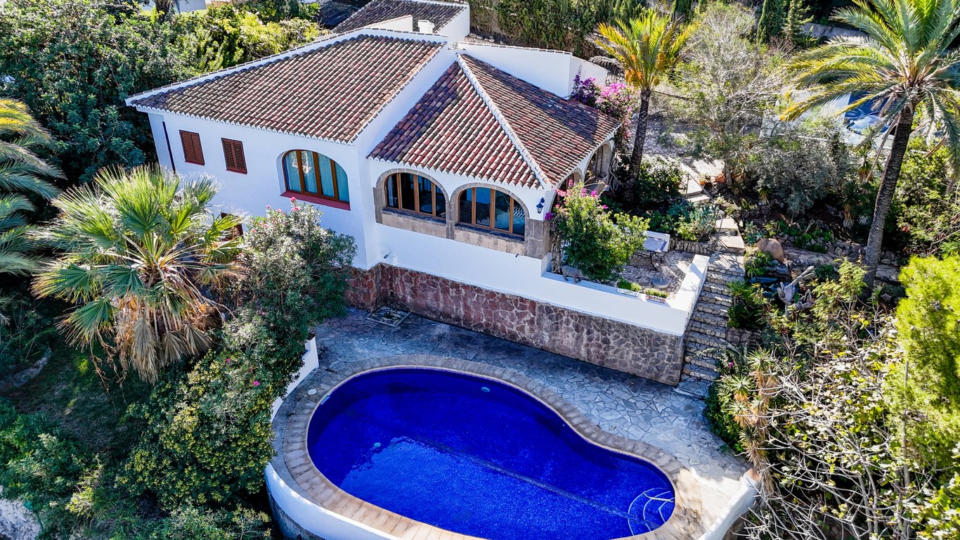 Aerial view of the villa featuring a kidney-shaped pool, white facade with stone cladding, and a glazed naya with traditional Tosca stone arches.