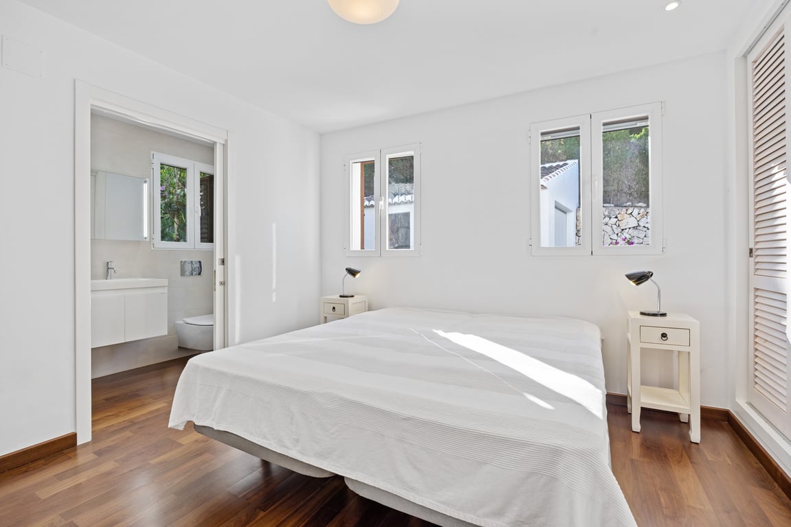 Bright bedroom featuring warm wood flooring, a modern en-suite bathroom, and double-glazed windows that fill the space with natural light.