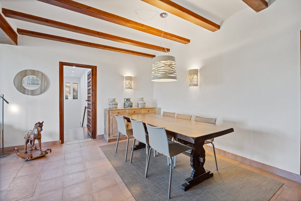 Dining area featuring exposed wooden ceiling beams, traditional ceramic tile flooring, and a solid wood table complemented by modern lighting fixtures.