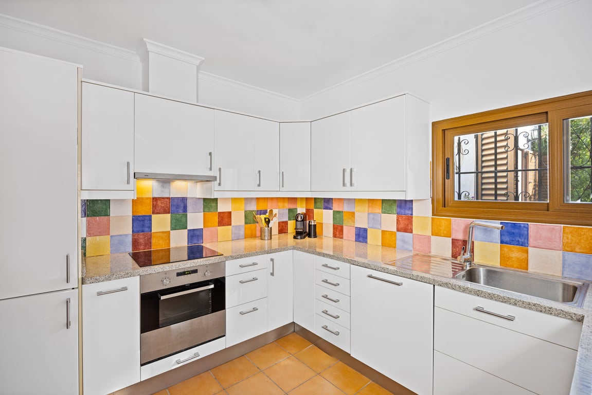 Equipped kitchen featuring white cabinetry, granite countertops, and a vibrant handmade ceramic tile backsplash. Includes an integrated oven and wood-framed window.