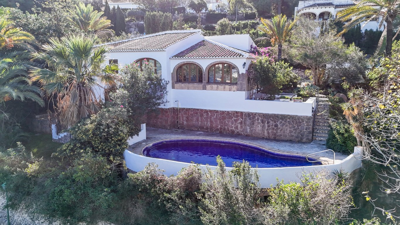 Exterior view of the villa featuring an oval private pool, natural stone retaining walls, and a traditional naya with Tosca stone arches.