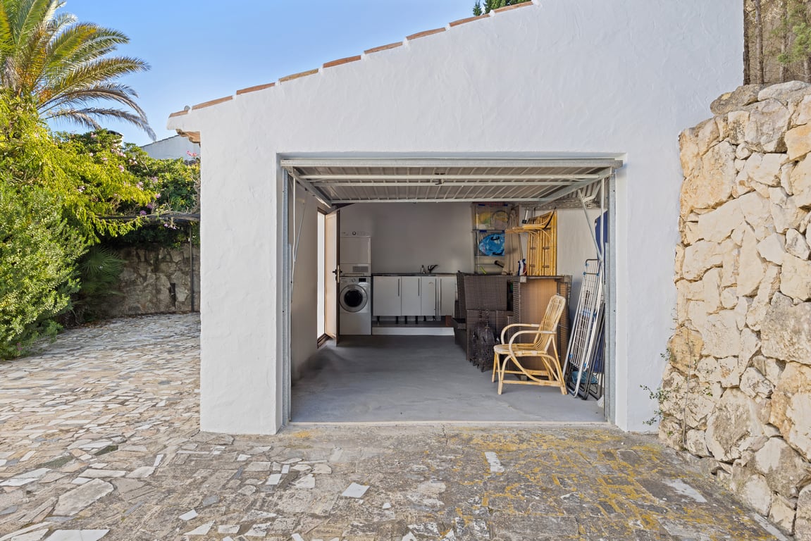 Functional garage and utility room featuring a laundry area with washer, dryer, and storage cabinets, adjacent to a natural stone wall and paved driveway.