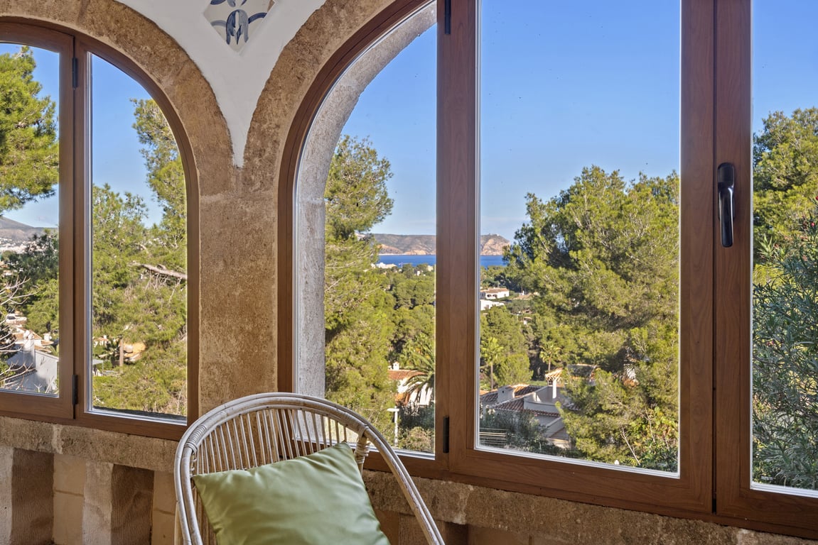 Glazed naya featuring original Tosca stone arches and wooden-framed windows overlooking the Mediterranean Sea and lush pine forests.