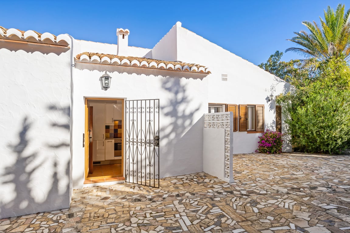 Mediterranean exterior with white-washed walls, irregular stone paving, and a secondary entrance featuring a wrought iron gate and traditional wooden window shutters.