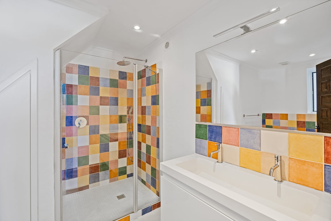 Modern bathroom featuring a double vanity sink and a glass-enclosed shower, accented by vibrant multi-colored ceramic tiling and recessed ceiling lights.