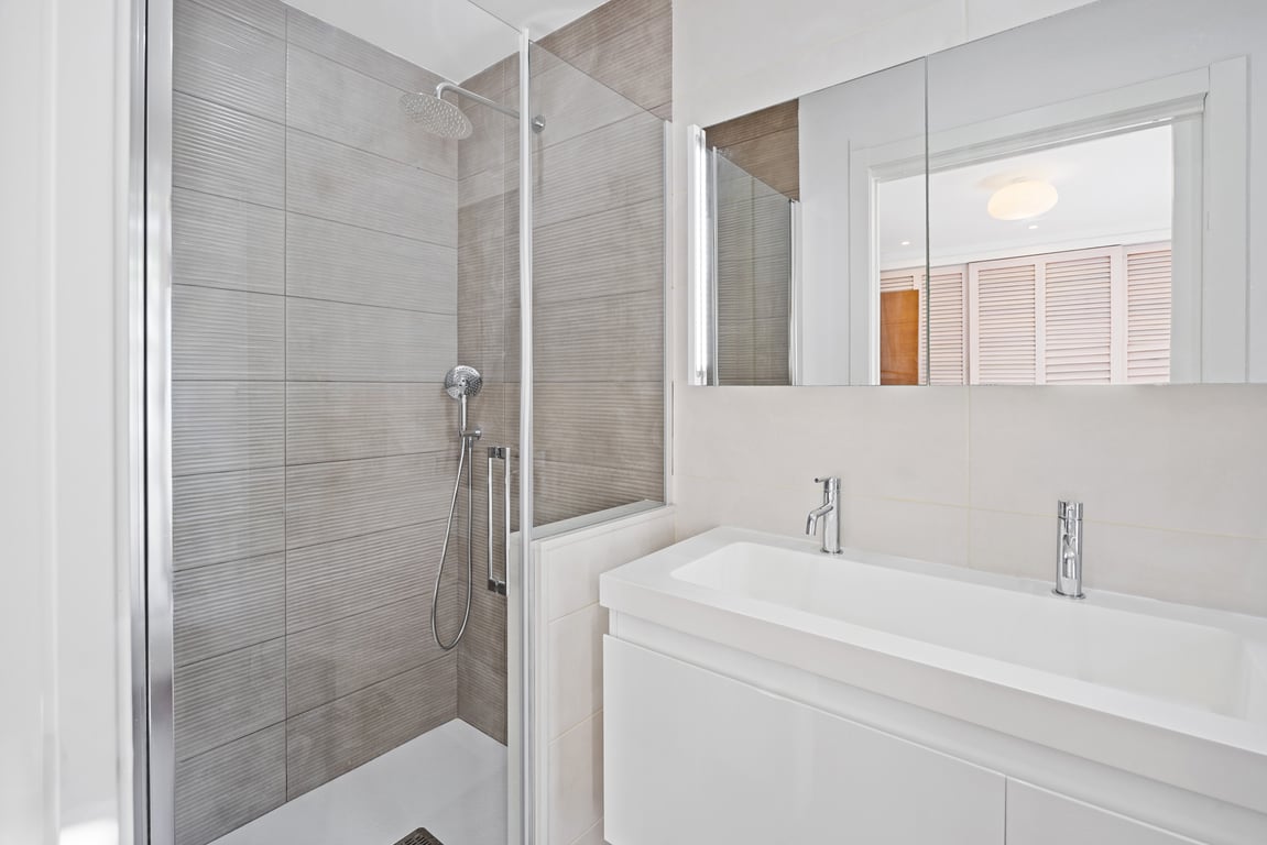Modern bathroom with a walk-in shower featuring textured grey tiles, a glass screen, and a sleek white vanity unit with minimalist chrome faucets.