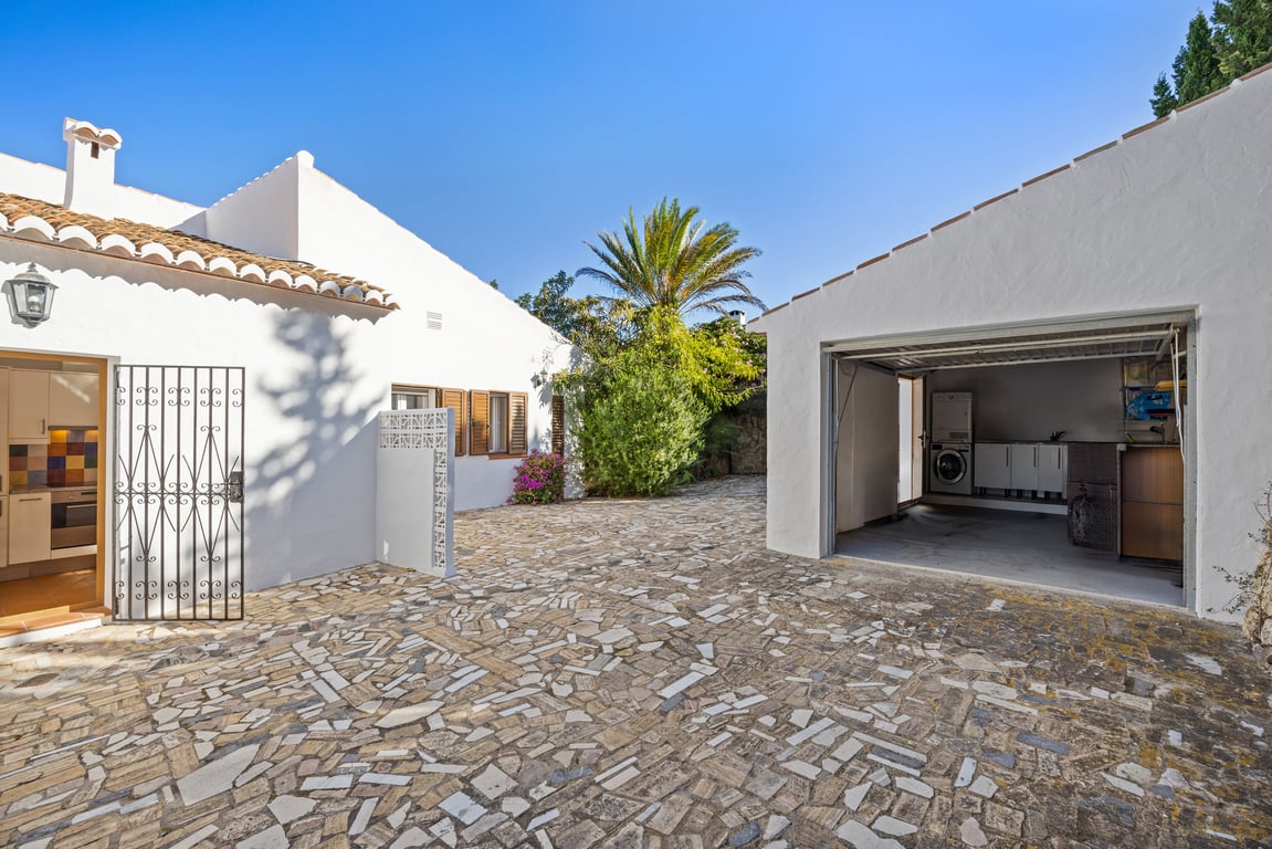 Stone-paved exterior courtyard featuring a kitchen entrance with a wrought-iron gate and a separate garage housing a functional laundry area.