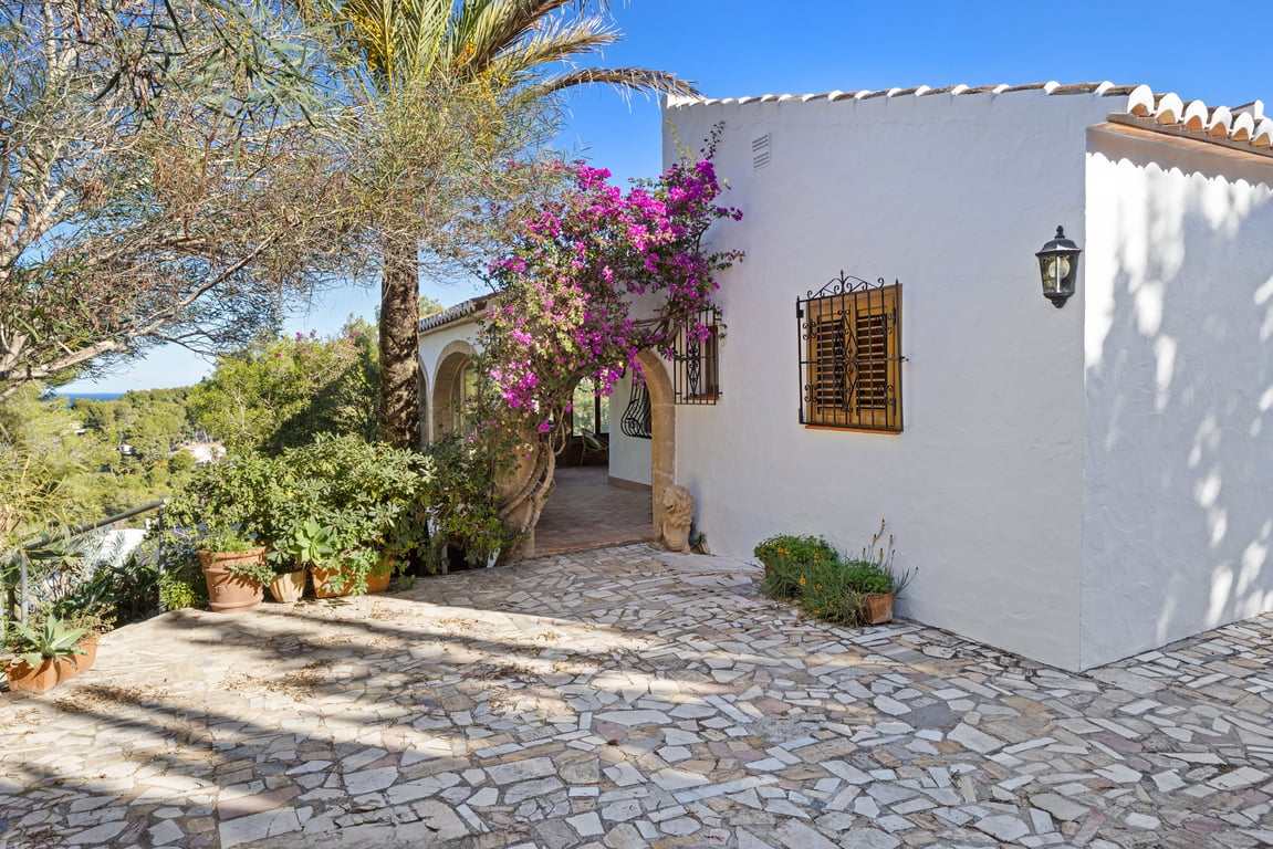 Traditional white facade featuring Tosca stone arches, blooming bougainvillea, and an irregular stone terrace overlooking the Mediterranean landscape.