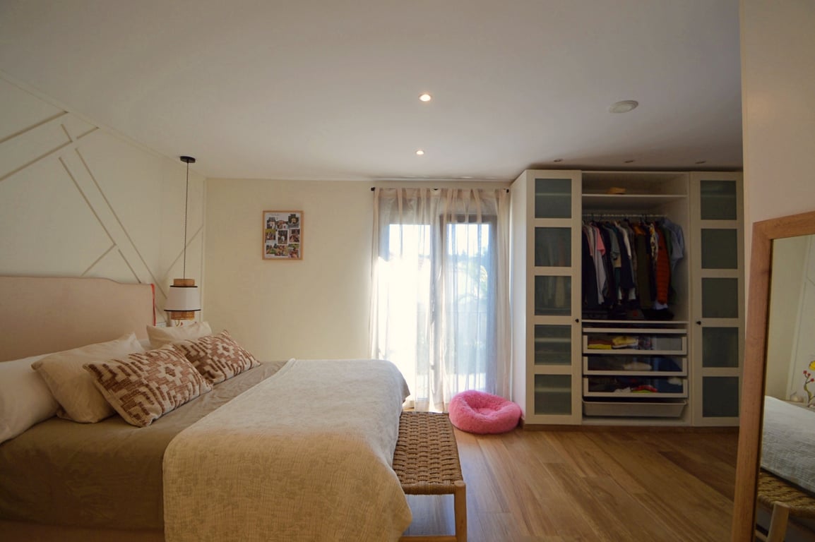 Bright bedroom featuring light wood floors, a geometric accent wall, and a built-in wardrobe with translucent glass panels and integrated storage.
