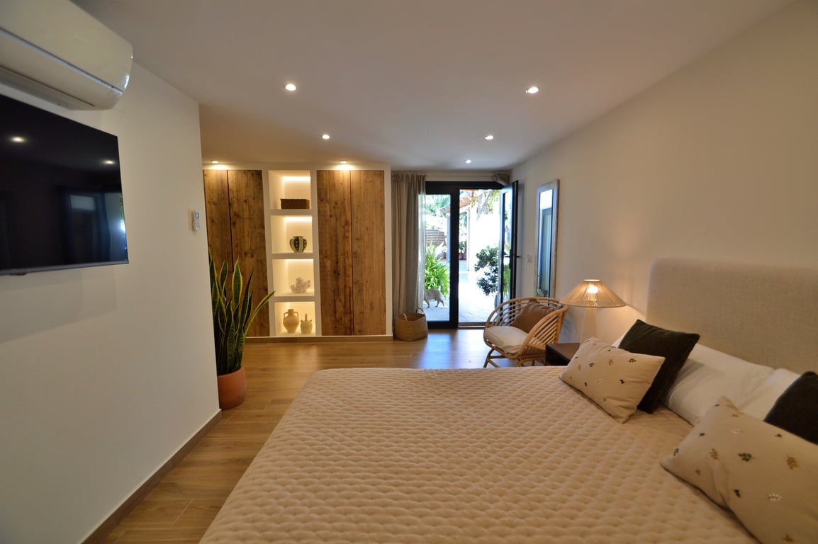 Bright bedroom featuring natural wood wardrobes with integrated backlit shelving, wood-effect flooring, and direct access to the outdoor terrace.