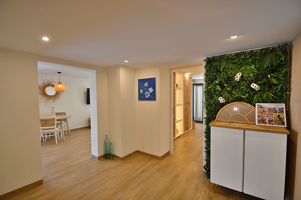 Bright hallway featuring wood-effect flooring, recessed lighting, and a decorative green wall next to a modern sideboard, connecting to the dining area.