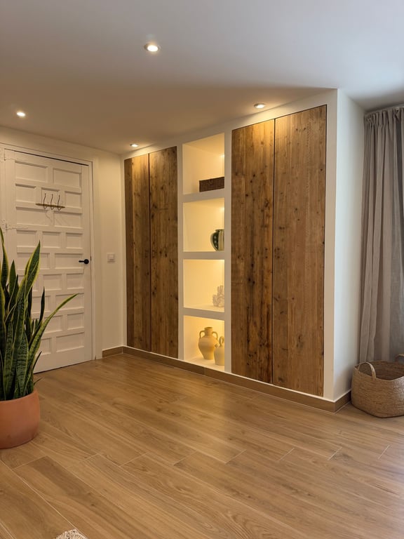 Built-in wardrobe featuring rustic wood doors and integrated LED-lit display shelving, complemented by wood-effect ceramic flooring and recessed spotlights.