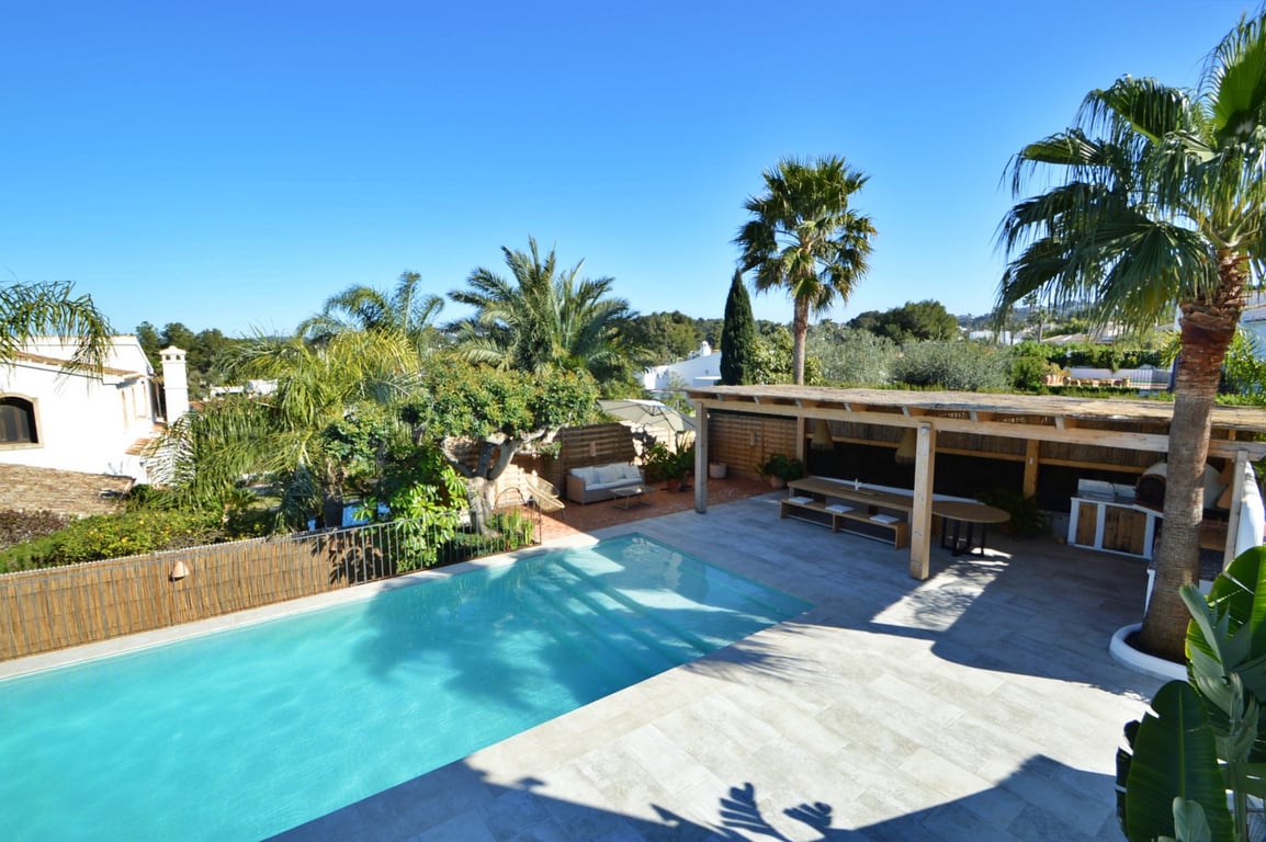 Elevated view of the saltwater pool and stone terrace, featuring a wooden pergola with an outdoor dining area and kitchen equipped with a pizza oven.