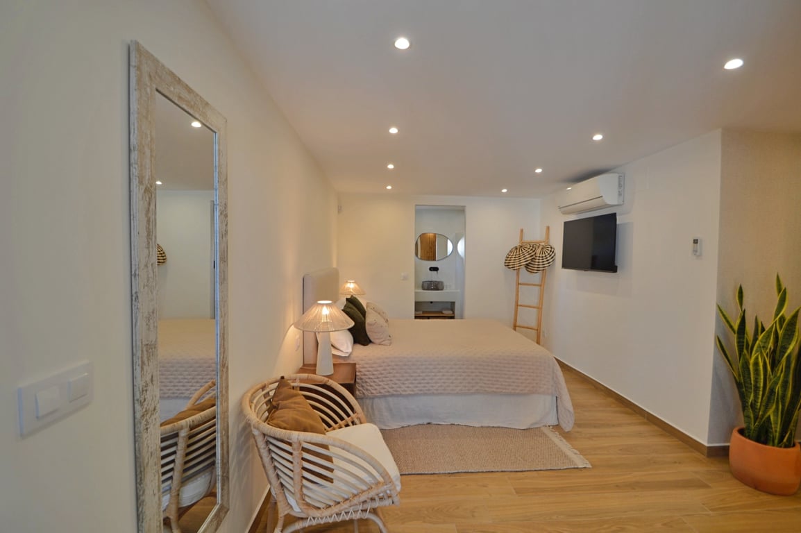 Ibizan-style bedroom featuring wood-effect flooring, recessed LED lighting, split air conditioning, and an integrated ensuite bathroom.
