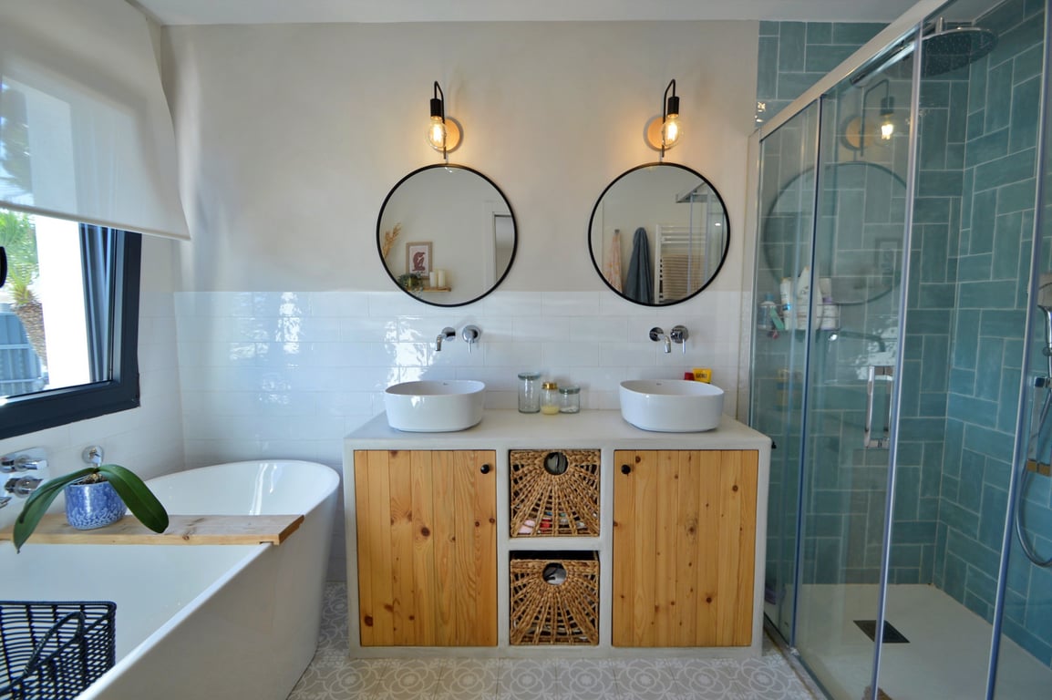 Modern bathroom featuring a double vanity with wooden accents, a freestanding bathtub, and a walk-in shower with vibrant turquoise tiling and glass enclosure.