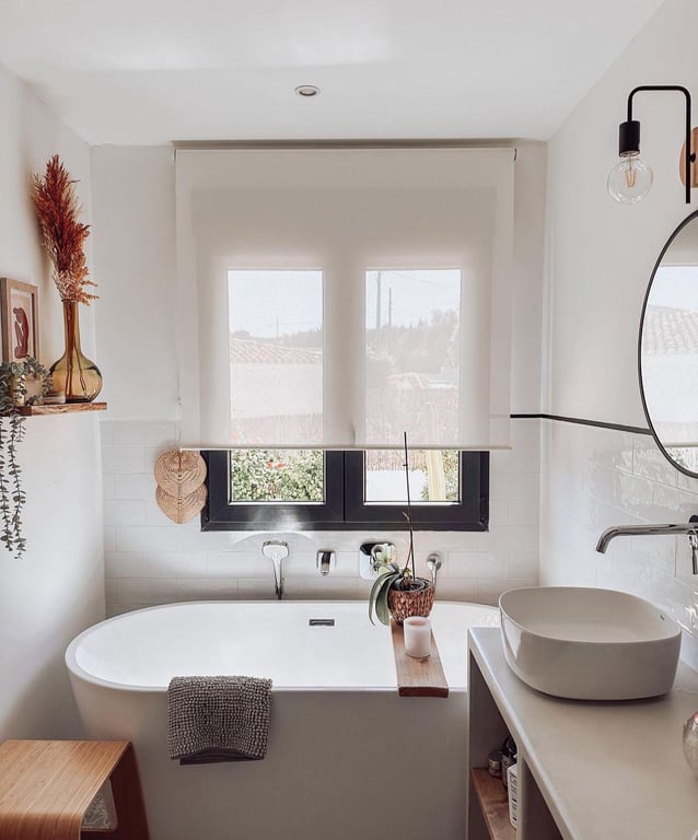 Modern bathroom featuring a freestanding oval tub, vessel sink, and black-framed window. White subway tiles and natural wood accents define the Ibizan style.