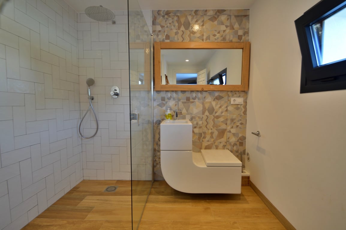 Modern bathroom featuring a walk-in shower with glass screen and a unique integrated sink-toilet unit. Includes geometric accent tiling and a large wood-framed mirror.