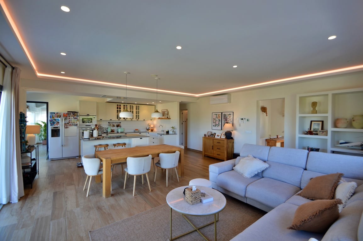 Open-concept living and dining area featuring a modern kitchen with island, recessed LED ceiling lighting, and light wood flooring throughout.