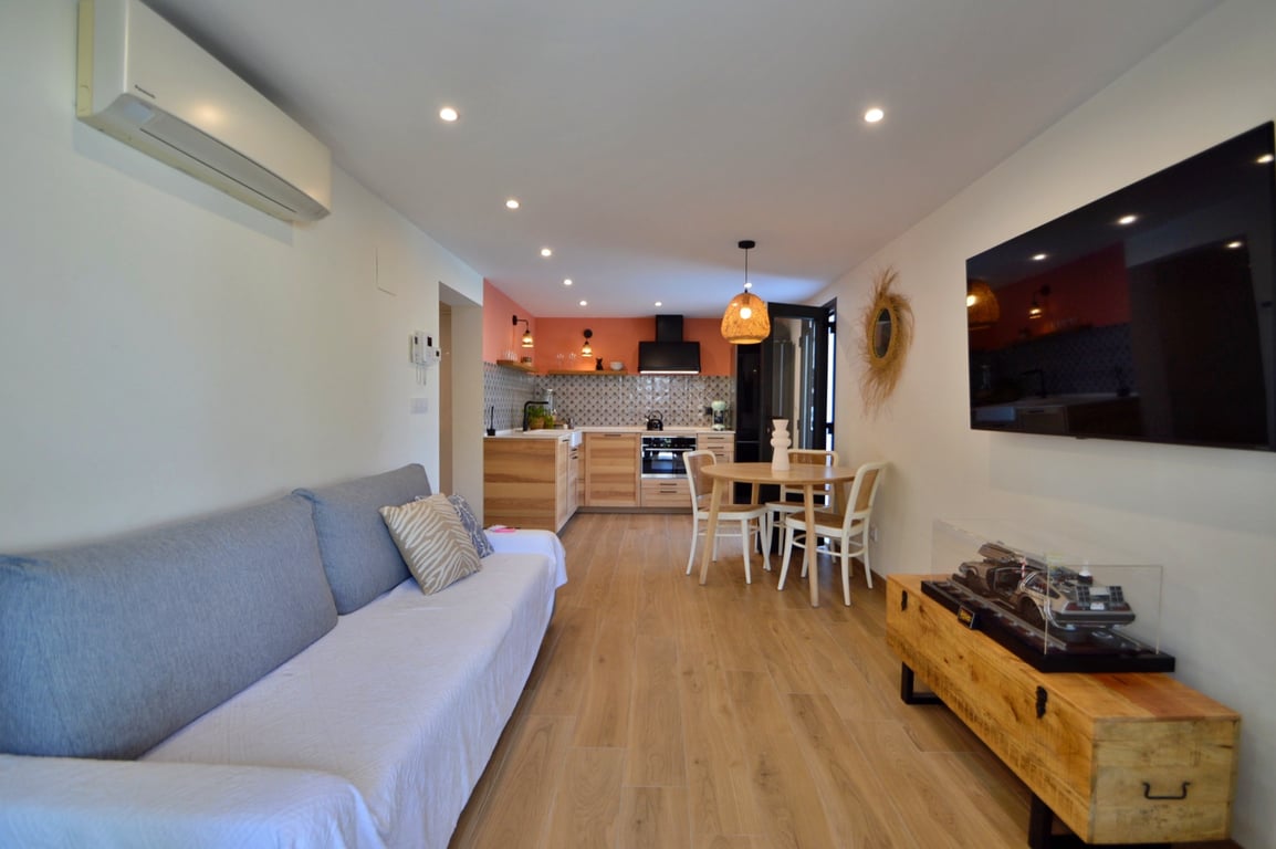Open-plan living and dining area featuring an integrated kitchen with wooden cabinetry, recessed lighting, and a wall-mounted television.