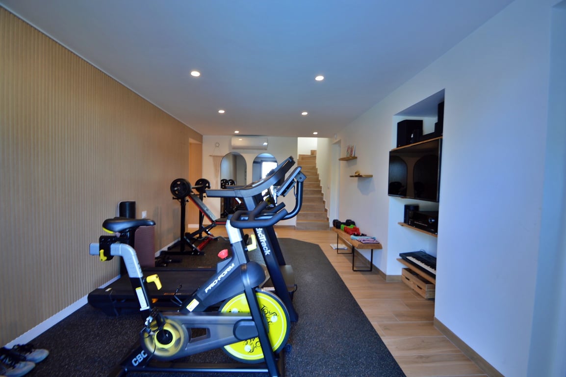 Private home gym featuring a spinning bike, treadmill, and weight area, complete with wood-paneled walls, recessed lighting, and integrated multimedia shelving.