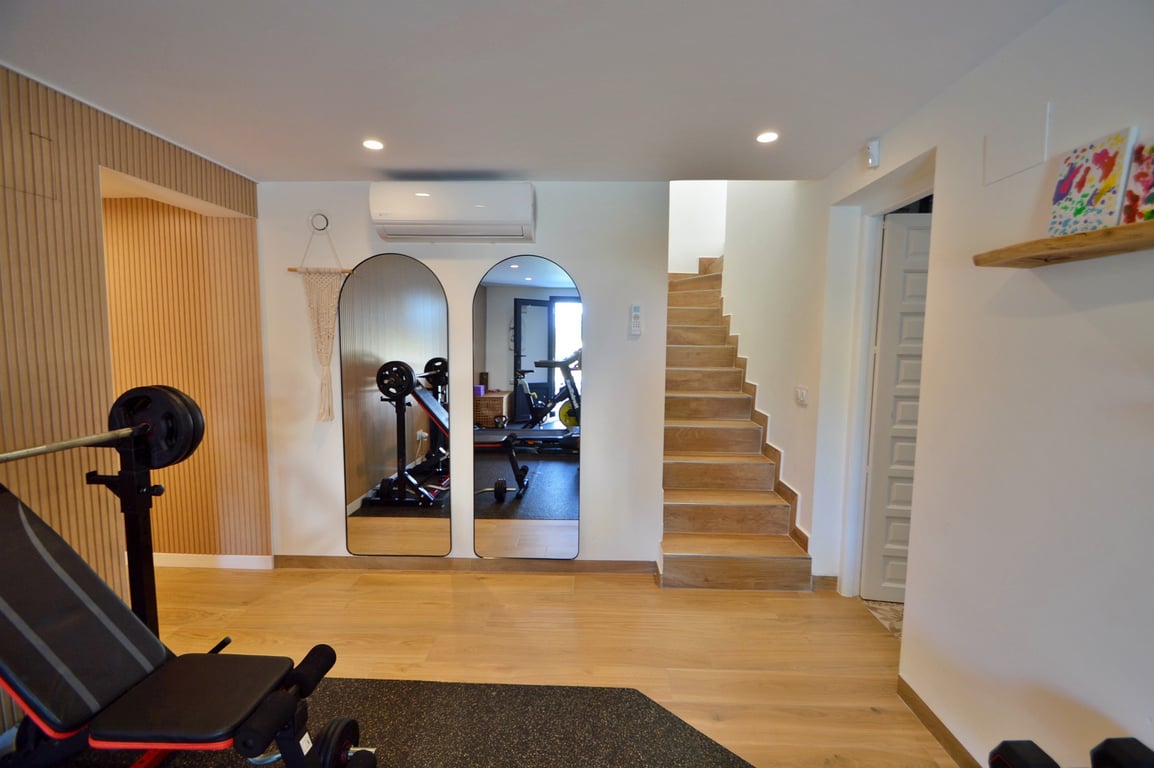 Private home gym featuring arched mirrors, wood-effect flooring, wall-mounted air conditioning, and a staircase connecting to the upper floor.