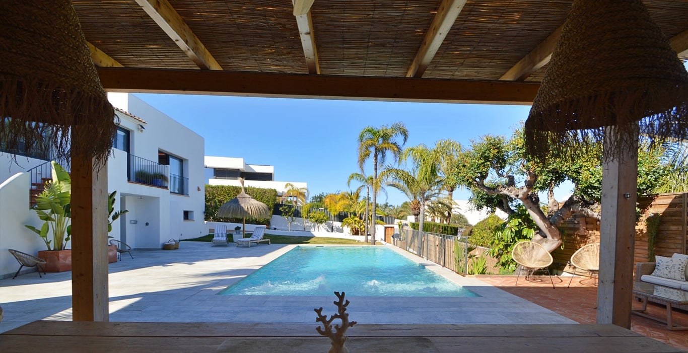 View from the shaded terrace with a bamboo roof overlooking the saltwater pool, sun deck, and landscaped Mediterranean garden.