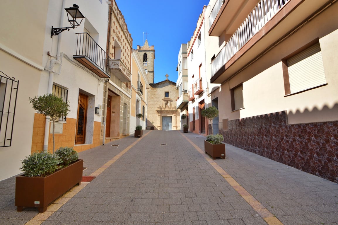 Exterior view of a paved pedestrian street leading to a historic stone church, flanked by traditional townhouses with wrought iron balconies.