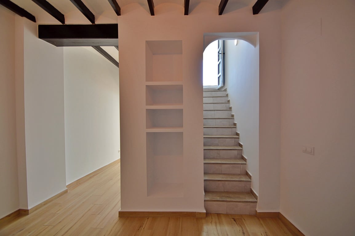 Interior hallway featuring exposed dark wood beams, built-in wall niches, and a tiled staircase leading to the upper level with natural light.