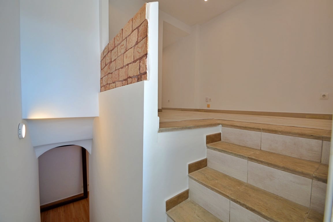 Interior staircase featuring wood-effect ceramic tiles, white walls, and a decorative brick accent wall separating the split-level landing.
