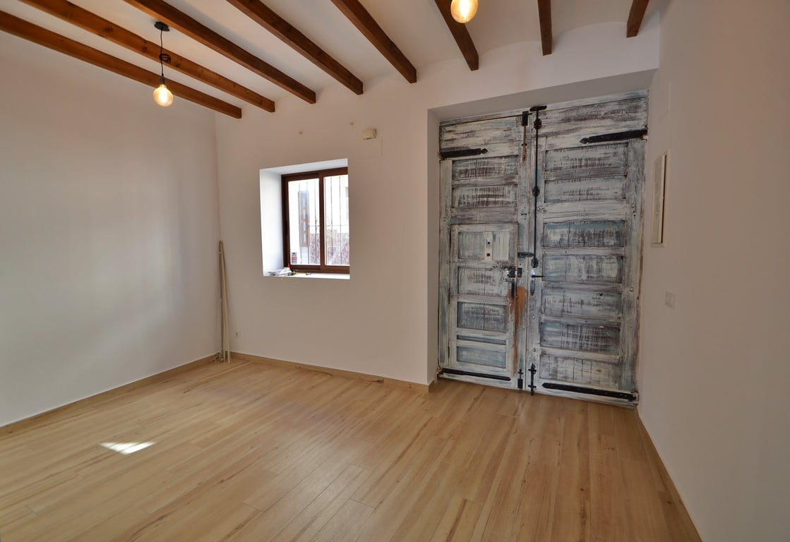 Main entrance featuring restored rustic wooden double doors, exposed ceiling beams, and light wood flooring in a bright, minimalist space.