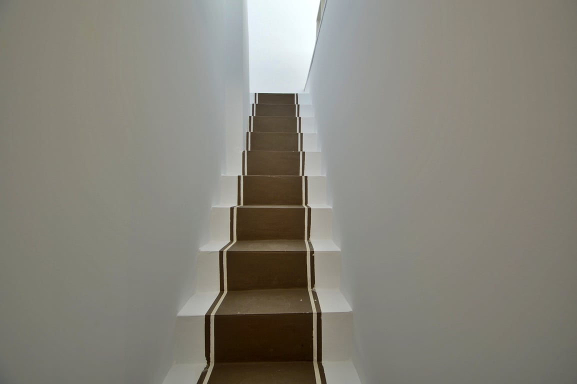 Minimalist interior staircase featuring brown painted steps with white borders, illuminated by natural light from above.