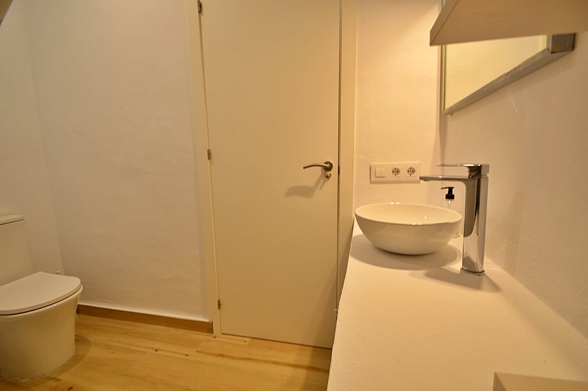 Modern bathroom featuring a white vessel sink, chrome faucet, and light wood flooring. The minimalist design is complemented by white walls and contemporary fixtures.