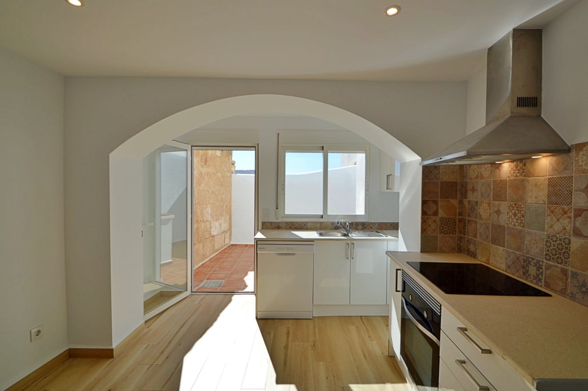 Modern kitchen featuring a white archway, decorative tile backsplash, and direct access to a private sunlit patio with traditional terracotta flooring.