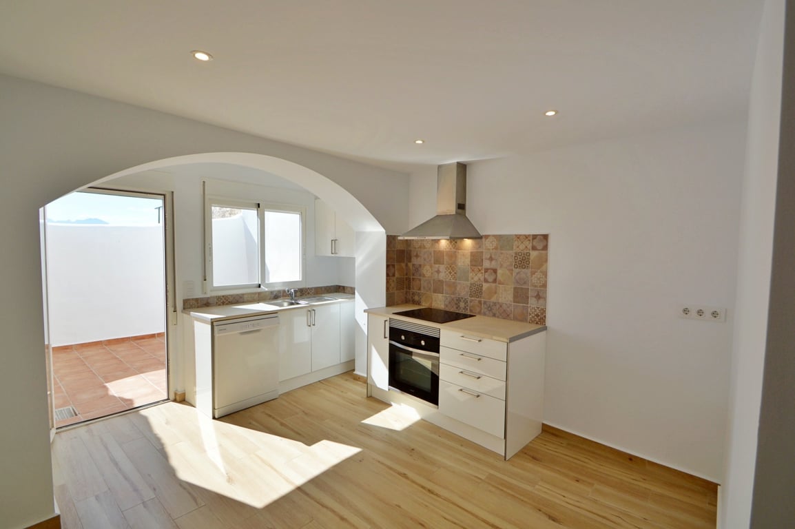 Modern renovated kitchen featuring white cabinetry, patterned tile backsplash, and direct access to a private sunlit patio.
