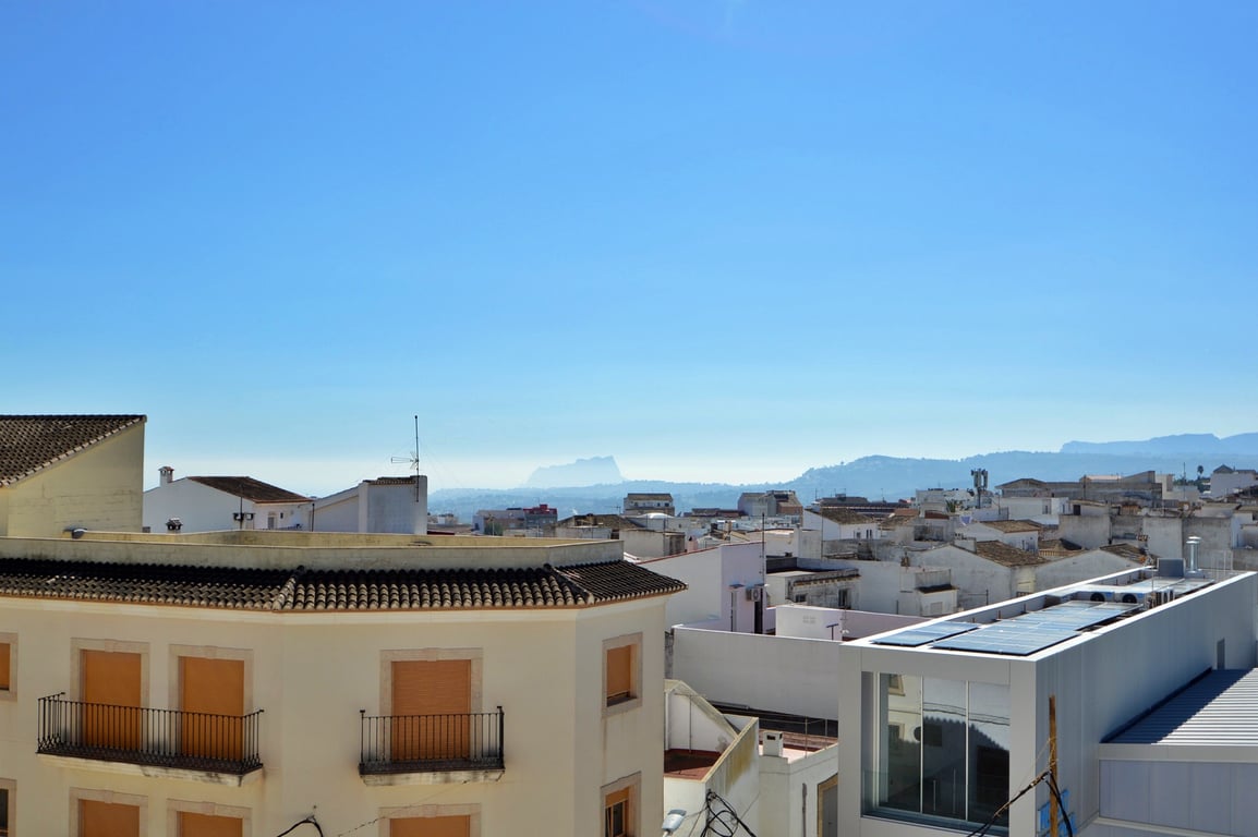 Panoramic views from the terrace overlooking village rooftops, featuring distant mountain silhouettes and the Mediterranean Sea horizon under a clear blue sky.