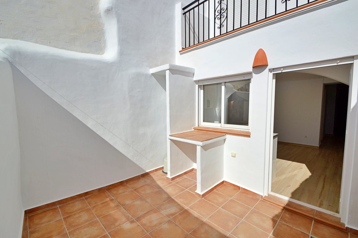 Private patio featuring traditional terracotta floor tiles, whitewashed walls, and a built-in outdoor counter. A sliding glass door connects the space to the interior.
