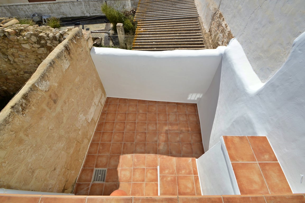 Private terrace featuring terracotta floor tiles, whitewashed walls, and an original stone masonry wall that preserves the building's authentic character.