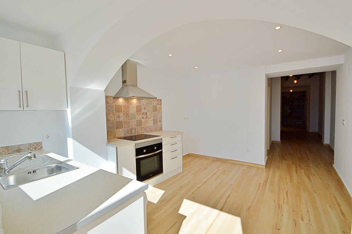 Renovated kitchen with white cabinetry, patterned tile backsplash, and integrated appliances. Features light wood flooring, recessed lighting, and a structural archway.