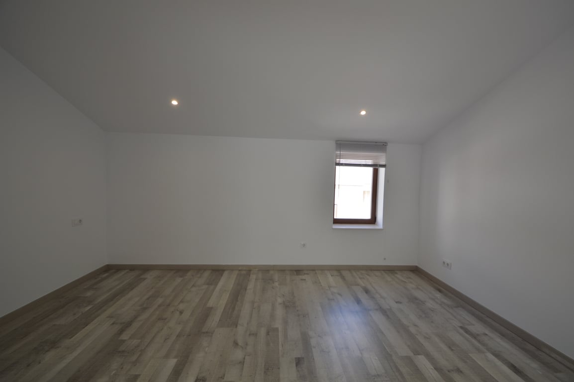 Renovated room featuring light wood-effect flooring, smooth white walls, recessed ceiling spotlights, and a window with a venetian blind.