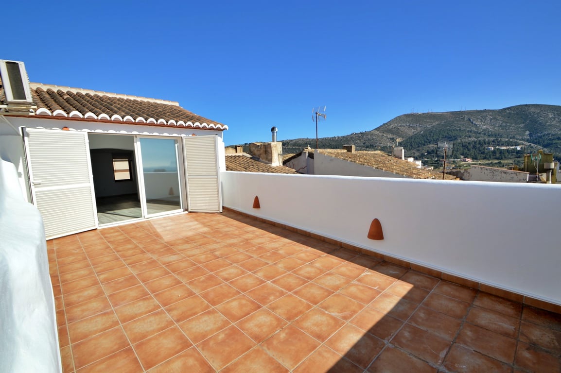 Spacious roof terrace featuring terracotta tiling, white perimeter walls with integrated lighting, and panoramic mountain views.
