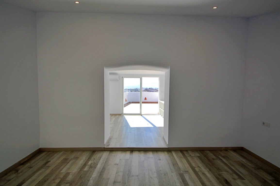 Versatile interior room featuring wood-effect flooring, recessed ceiling lights, and an arched doorway leading to a sunlit area with terrace access.