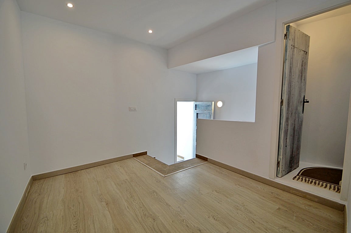 Versatile intermediate room featuring light wood-effect flooring, recessed ceiling spotlights, and a characterful distressed wooden door.
