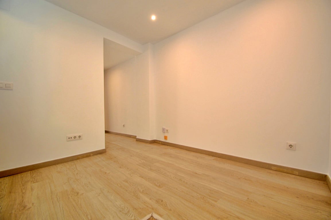 Versatile renovated interior room featuring light wood-effect laminate flooring, smooth white walls, and recessed ceiling spotlights.