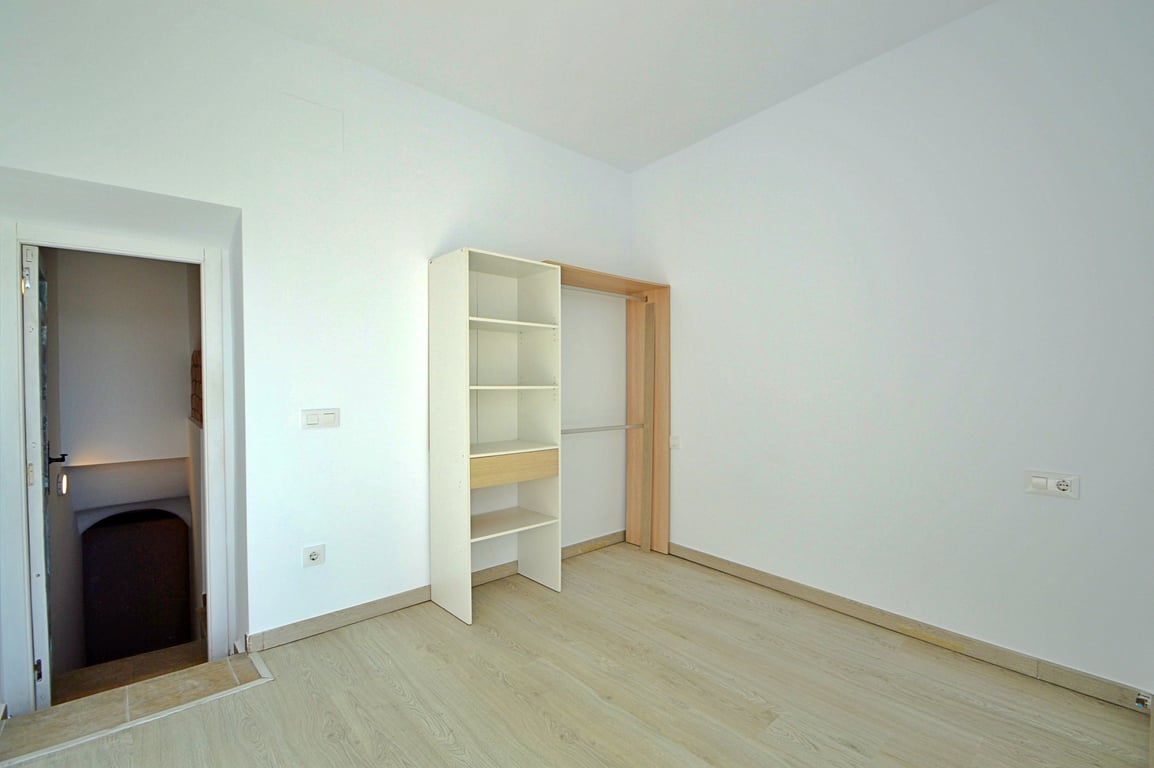Versatile room featuring light wood-effect flooring, white walls, and an open shelving unit with a hanging rail, located adjacent to the staircase.