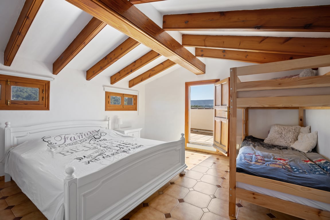 Attic bedroom featuring exposed wooden beams, terracotta tile flooring, and direct access to a private terrace. The space includes a double bed and wooden bunk beds.