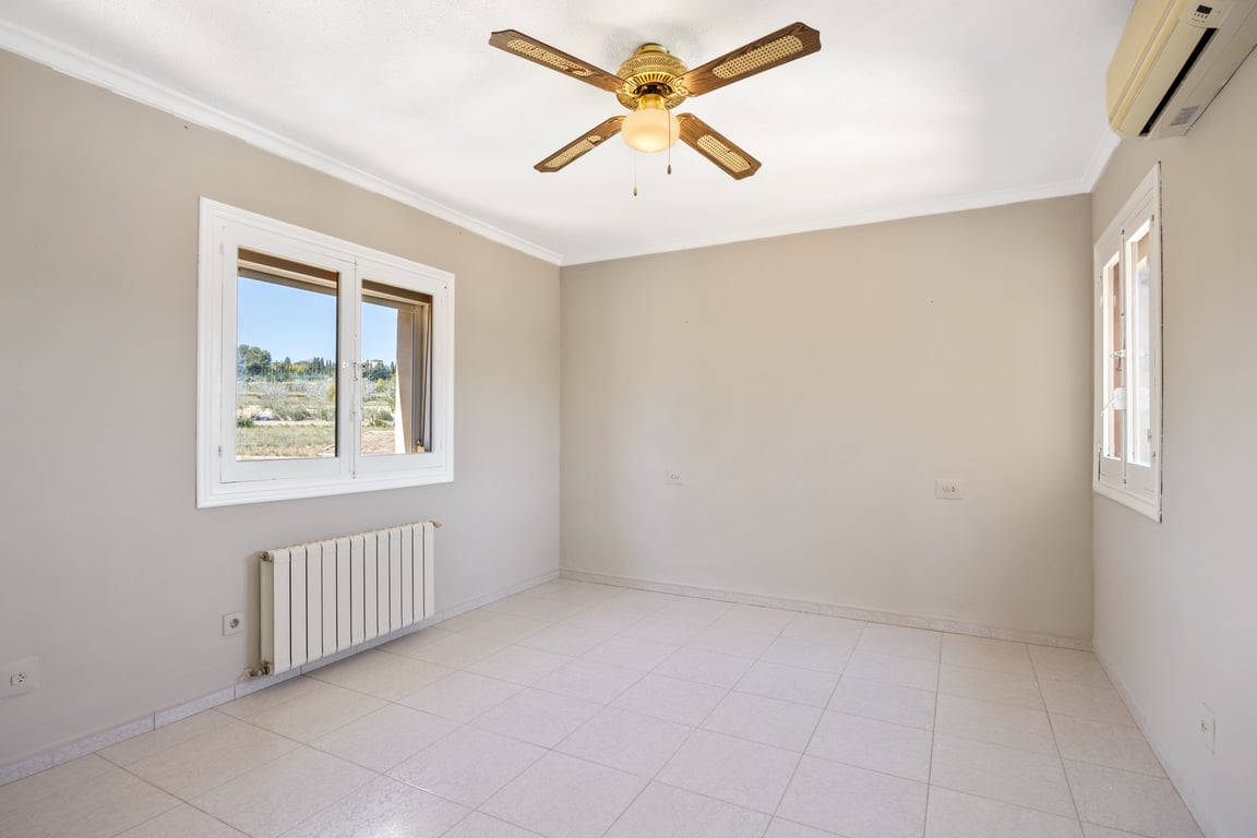 Bright bedroom featuring tiled flooring, a classic ceiling fan, air conditioning, and central heating. Dual-aspect windows provide natural light and countryside views.