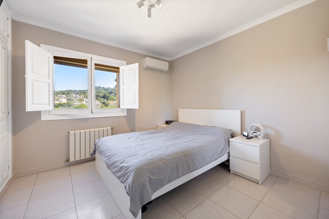 Bright bedroom featuring white shutters, air conditioning, and open views of the Jávea landscape. Finished with neutral tones and ceramic tile flooring.