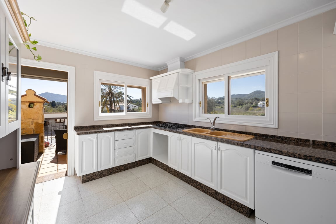 Bright kitchen featuring white cabinetry, dark granite countertops, and scenic countryside views through large windows. Includes direct terrace access.