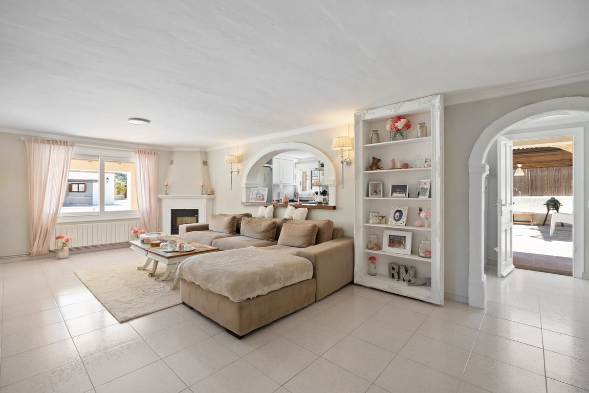 Bright living area featuring a corner fireplace, modular sofa, and arched openings to the kitchen and terrace. Includes custom decorative shelving and tiled flooring.